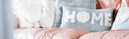 Image of a pillow which says HOME on a pick couch will several other pillows